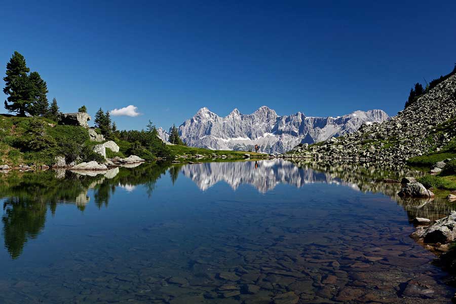 Meditationsgruppe in der Almhütte: „Teilnehmer praktizieren stille Meditation in der rustikalen Almhütte des Almdorf Winkl.“ Miriam beim Anleiten: „Yoga-Lehrerin Miriam führt eine geführte Meditation vor atemberaubender Bergkulisse.“ Natur & Achtsamkeit: „Meditationskissen in der Wiese vor dem Almdorf Winkl, umgeben von Bergen und frischer Bergluft.“
