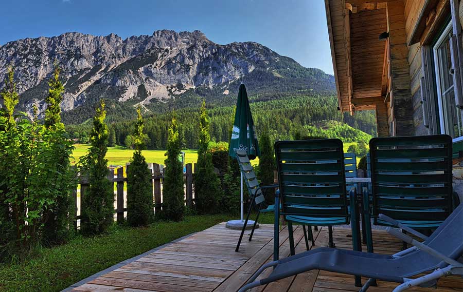 Almhütte außen im Sommer:
„Traditionelle Almhütte im Hüttendorf des Almdorf Winkl, umgeben von grünen Wiesen und Bergpanorama.“