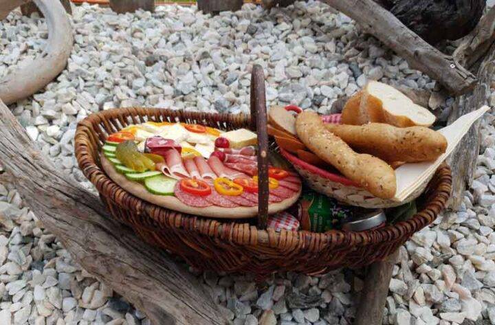 Frühstückskorb Gesamt: „Liebevoll gefüllter Frühstückskorb mit Wurst, Käse und Marmelade auf Holztisch im Almdorf Winkl“ Steierkas: „Nahaufnahme des regionalen Steierkas im Frühstückskorb“ Marmeladenauswahl: „Hausgemachte Erdbeer-, Himbeer- und Aprikosenmarmeladen im Almdorf Winkl“
