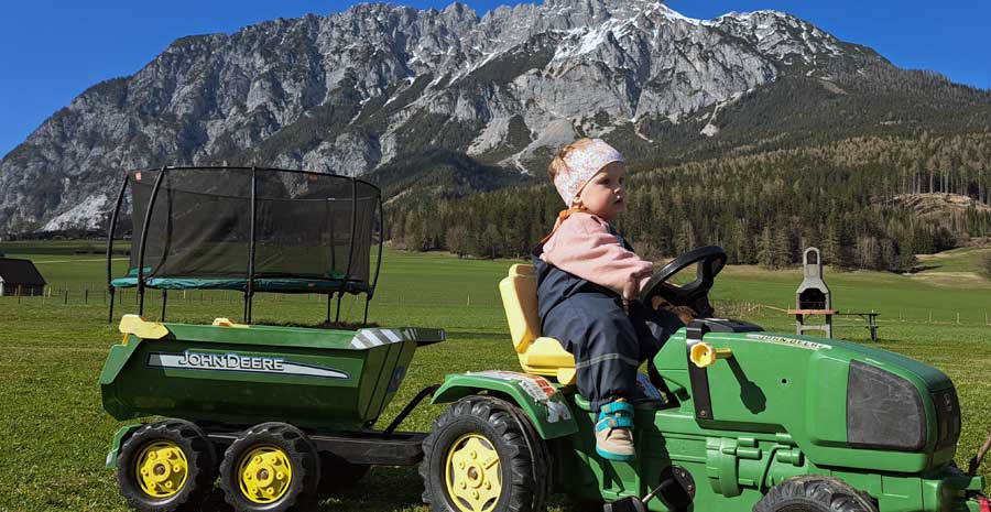 Mädchen namens Lilly fährt auf einem Kindertraktor am Spielplatz entlang