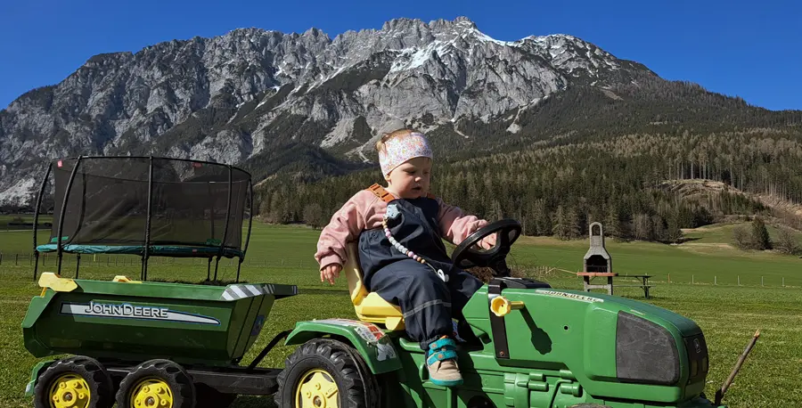 M&auml;dchen namens Lilly f&auml;hrt auf einem Kindertraktor am Spielplatz entlang