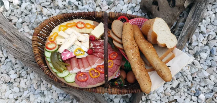 Frühstückskorb Gesamt: „Liebevoll gefüllter Frühstückskorb mit Wurst, Käse und Marmelade auf Holztisch im Almdorf Winkl“ Steierkas: „Nahaufnahme des regionalen Steierkas im Frühstückskorb“ Marmeladenauswahl: „Hausgemachte Erdbeer-, Himbeer- und Aprikosenmarmeladen im Almdorf Winkl“