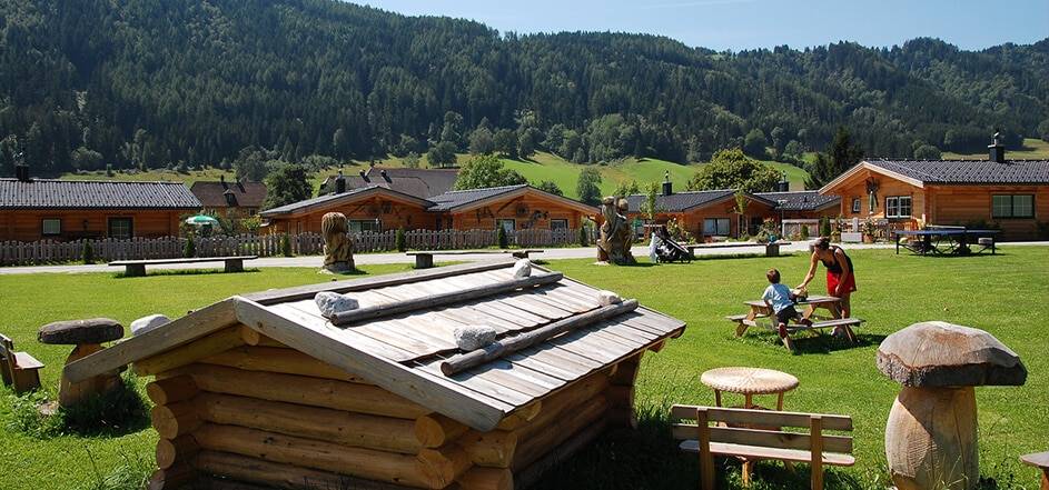 Almhütte außen im Sommer:
„Traditionelle Almhütte im Hüttendorf des Almdorf Winkl, umgeben von grünen Wiesen und Bergpanorama.“